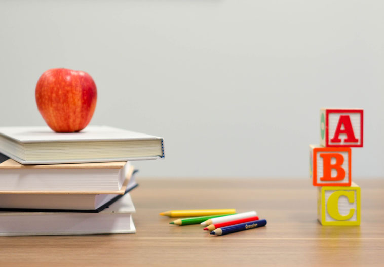 Schreibtisch mit Bücherstapel, Apfel, Stiften und Bauklötzen